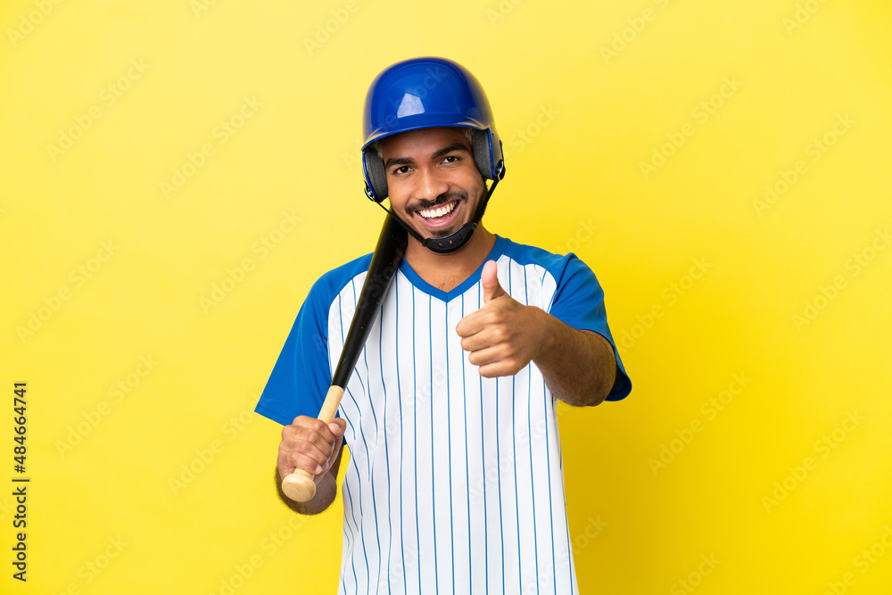 Young Colombian latin man playing baseball isolated on yellow background with thumbs up because something good has happened