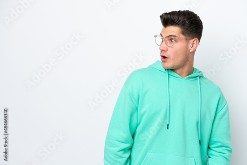 Young handsome caucasian man isolated on white bakcground doing surprise gesture while looking to the side © luismolinero
