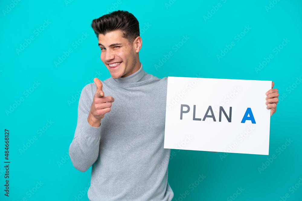 Young handsome caucasian man isolated on blue bakcground holding a placard with the message PLAN A and pointing to the front Young handsome caucasian man isolated on blue bakcground holding a placard with the message PLAN A and pointing to the front