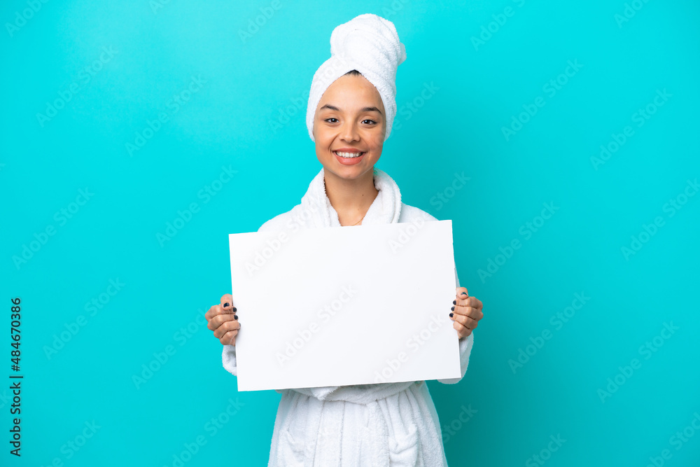 Young woman in a bathrobe with towel isolated on blue background holding an empty placard with happy expression Young woman in a bathrobe with towel isolated on blue background holding an empty placard with happy expression