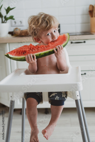 Adorable little boy eating juicy watermelon while sitting at the children's table