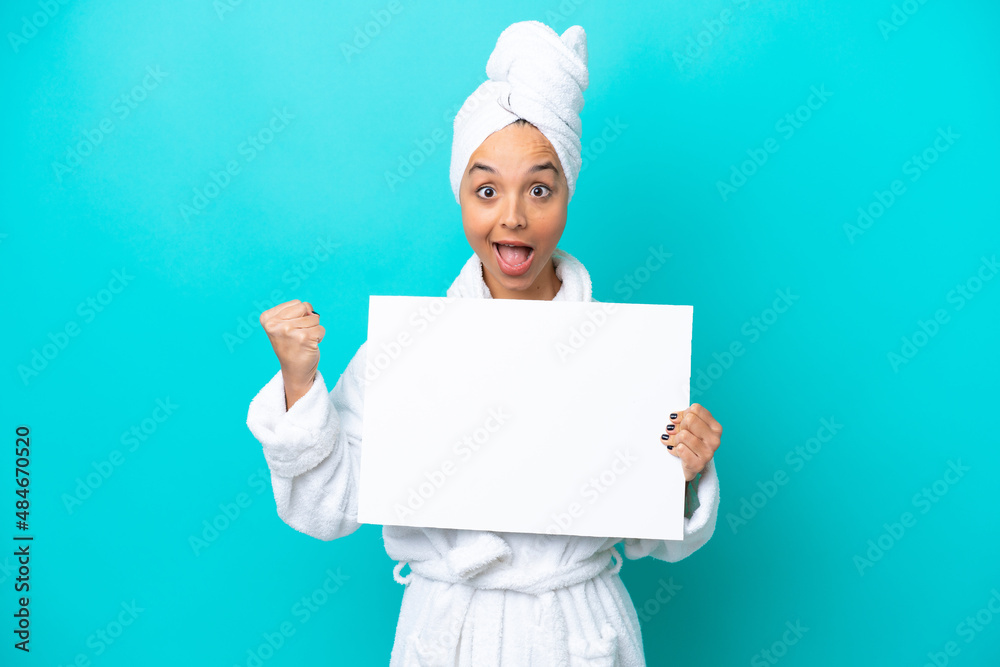 Young woman in a bathrobe with towel isolated on blue background holding an empty placard and celebrating a victory Young woman in a bathrobe with towel isolated on blue background holding an empty placard and celebrating a victory