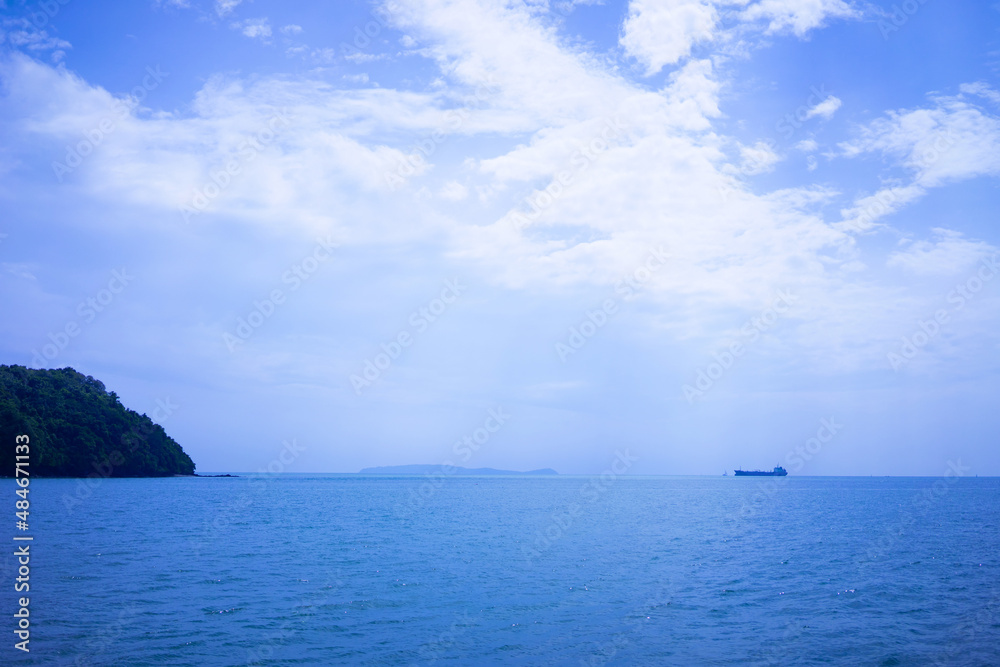 Obraz premium An island in the middle of the sea and a merchant ship is sailing in the sea.