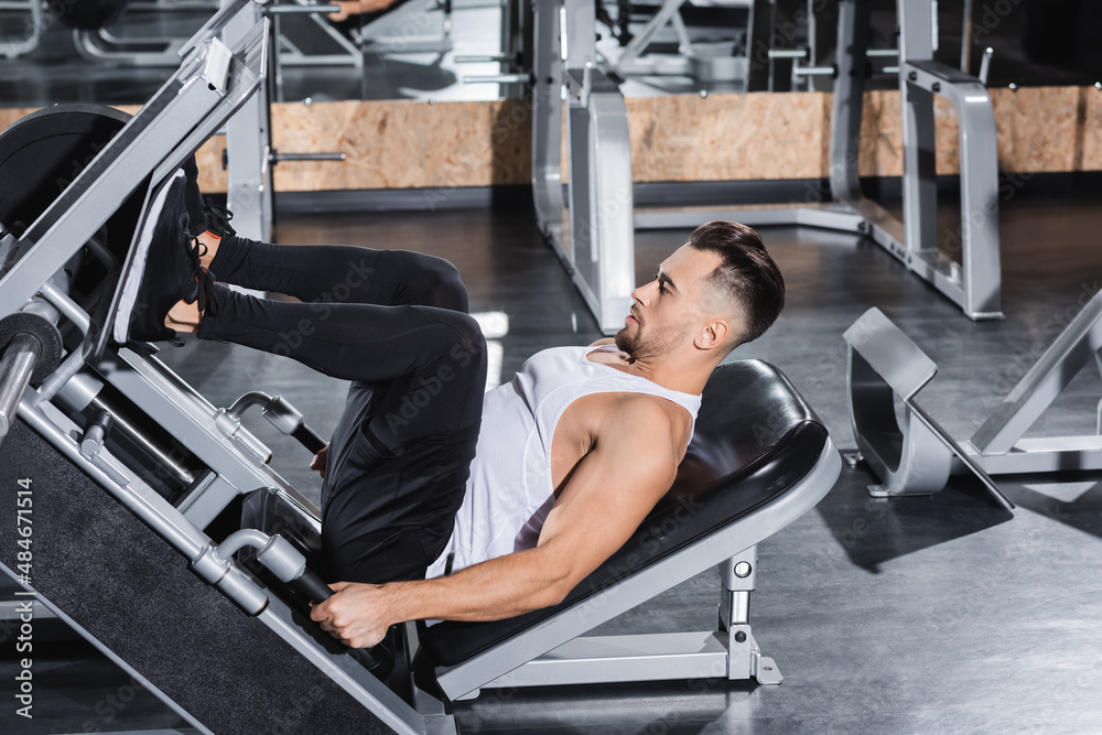 Stockfoto Side view of athletic sportsman training with leg press machine  in gym. | Adobe Stock