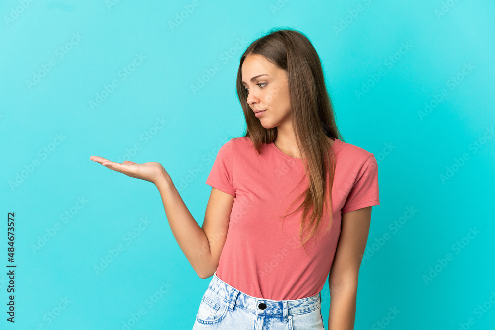Fototapeta premium Young woman over isolated blue background holding copyspace with doubts
