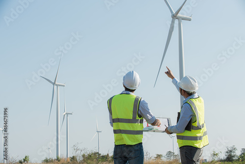 wind turbine worker. Back view of two engineers discussing against turbines on wind turbine farm.