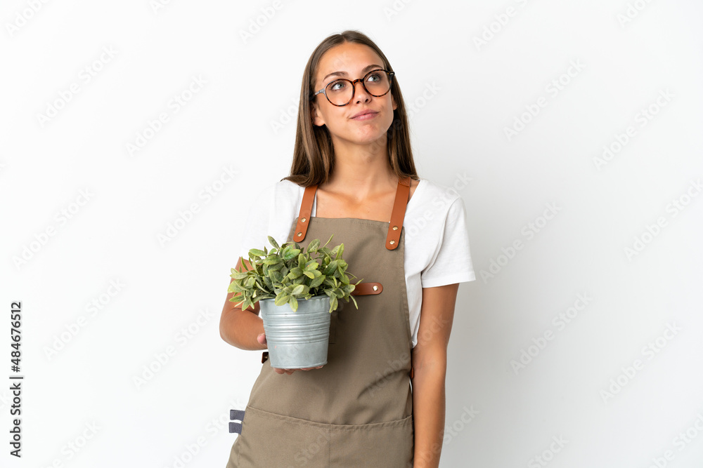 Gardener girl holding a plant over isolated white background and looking up Gardener girl holding a plant over isolated white background and looking up