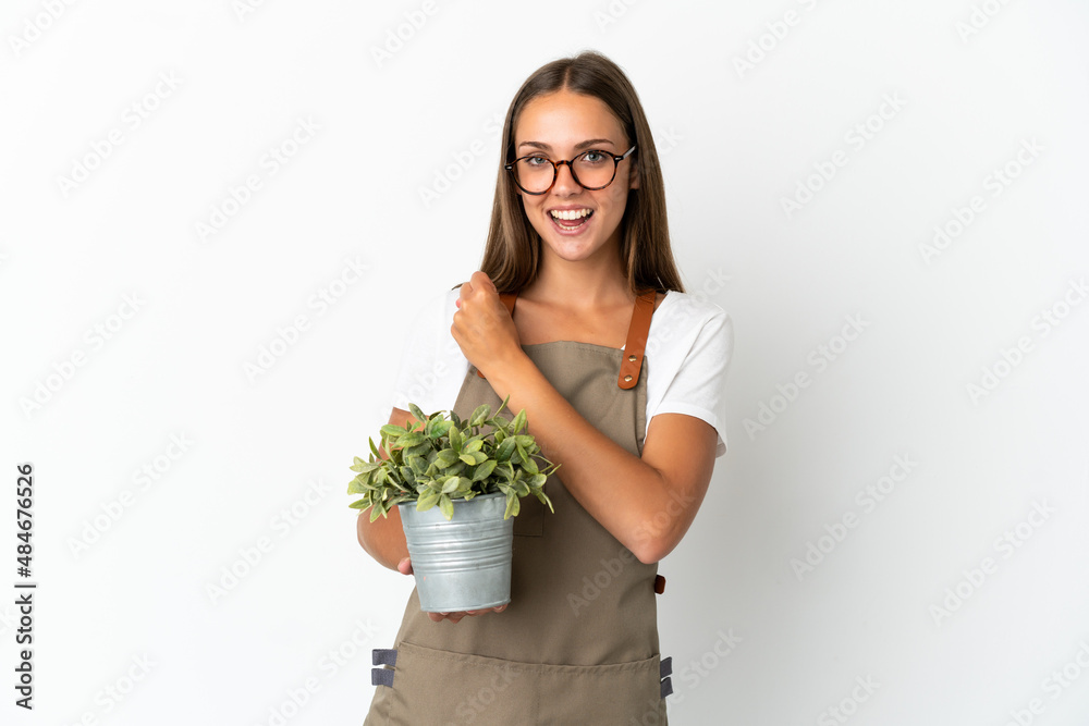 Gardener girl holding a plant over isolated white background celebrating a victory Gardener girl holding a plant over isolated white background celebrating a victory