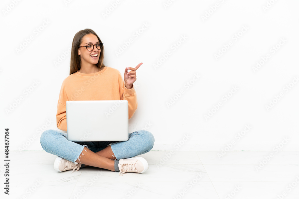 Young woman with a laptop sitting on the floor pointing finger to the side and presenting a product Young woman with a laptop sitting on the floor pointing finger to the side and presenting a product