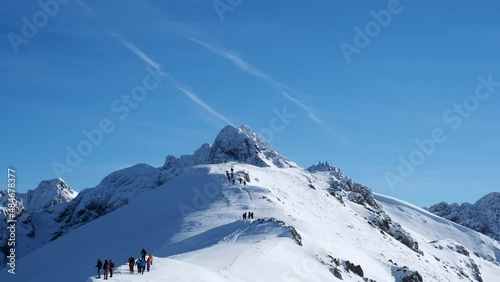 Group of people hikes high up in the snowy mountains in sunny day, travelling to mountains, active winter holidays, 4k 60p photo