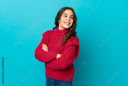 Little caucasian girl isolated on blue background with arms crossed and happy