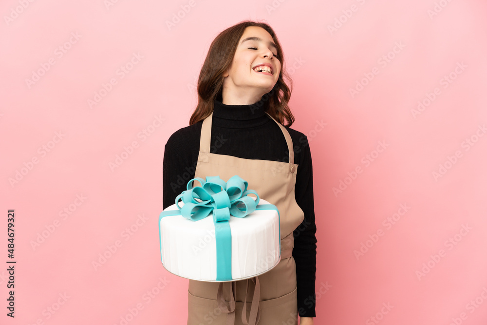 Little Pastry chef holding a big cake isolated on pink background laughing Little Pastry chef holding a big cake isolated on pink background laughing