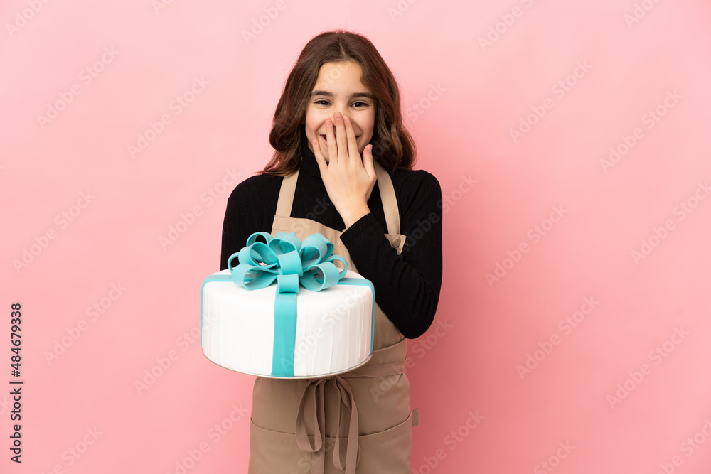 Little Pastry chef holding a big cake isolated on pink background happy and smiling covering mouth with hand Little Pastry chef holding a big cake isolated on pink background happy and smiling covering mouth with hand