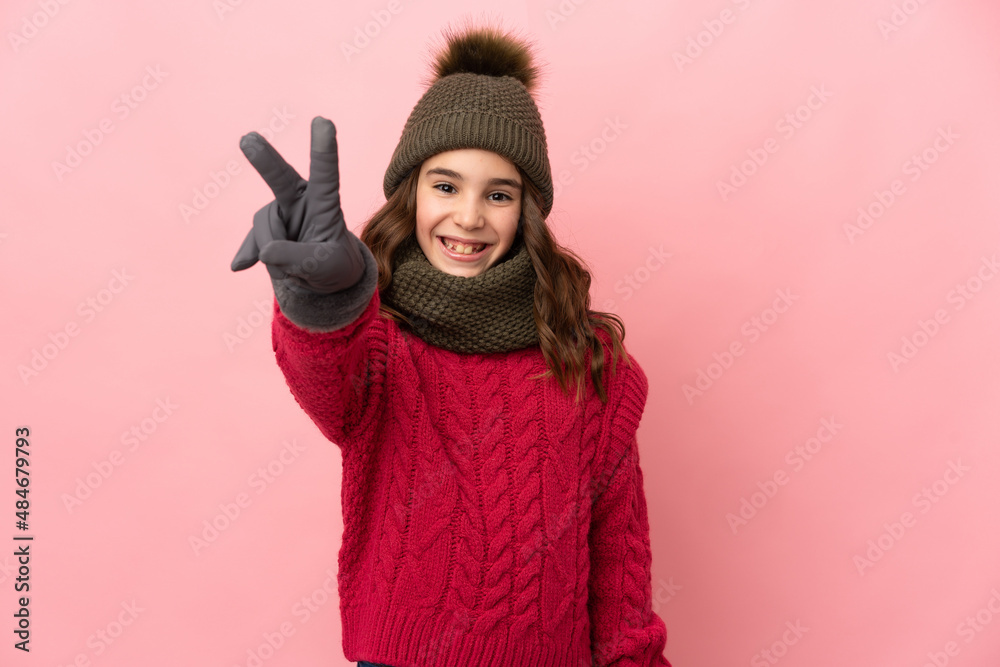 Little girl with winter hat isolated on pink background smiling and showing victory sign Little girl with winter hat isolated on pink background smiling and showing victory sign