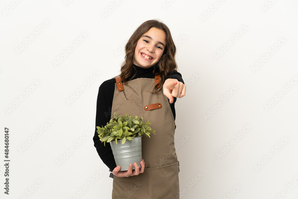 Little girl holding a plant isolated on white background pointing front with happy expression Little girl holding a plant isolated on white background pointing front with happy expression