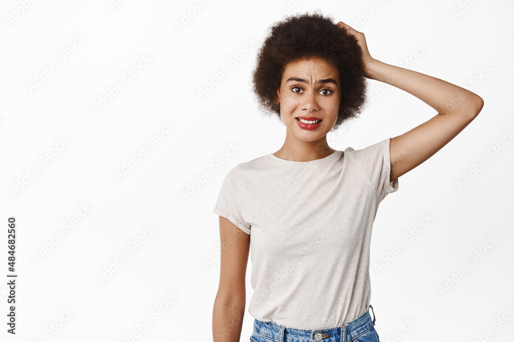 Image of freak out, confused young black woman scratching head, looking worried, indecisive, standing clueless against white background