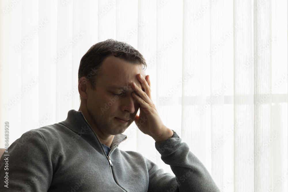 Tired man with closed eyes sitting near a window Tired man with closed eyes sitting near a window