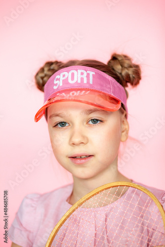 Photo of a girl with a happy positive smile, a sports tennis racket playing a game, isolated on a pink background