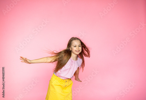 A funny little blonde girl of 10 years old in everyday bright clothes poses alone on a pink studio background. The concept of a child's lifestyle. The location of the copy space. Background for your t