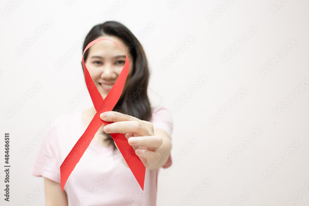 Asian woman are hold and present red ribbon in front of her face for AIDS campaign to encourage and caring patient. Asian woman are hold and present red ribbon in front of her face for AIDS campaign to encourage and caring patient.