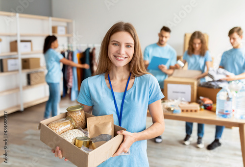 Obraz na płótnie Positive female volunteer in blue uniform holding cardboard box with food donati