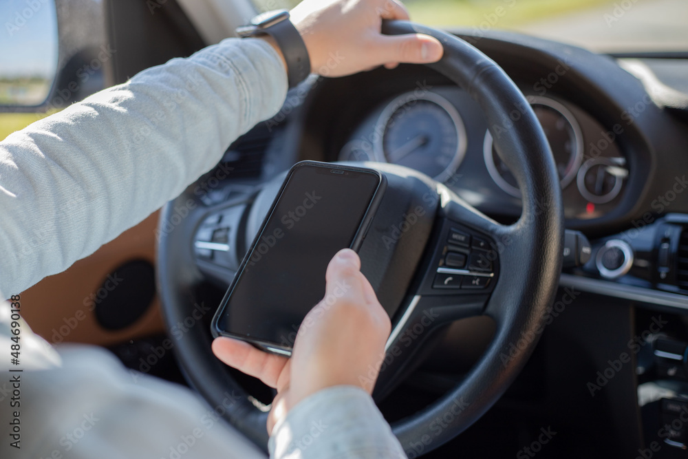 man using mobile smart phone inside a car. Driver hand holding blank black screen smartphone, searching address and pin location via map navigator application, transportation technology