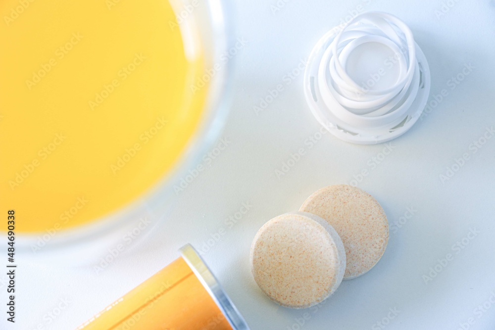 Fototapeta premium Vitamin C dissolvable tablets out of a tube on a white table, vitamin C drink in foreground, selective focus