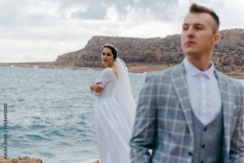 Portrait of happy newlyweds, bride and groom, standing on a rocky shore near the sea. A wonderful young couple Portrait of happy newlyweds, bride and groom, standing on a rocky shore near the sea. A wonderful young couple