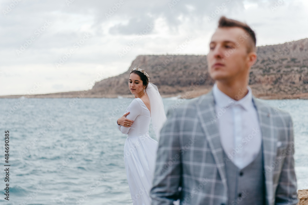 Portrait of happy newlyweds, bride and groom, standing on a rocky shore near the sea. A wonderful young couple Portrait of happy newlyweds, bride and groom, standing on a rocky shore near the sea. A wonderful young couple