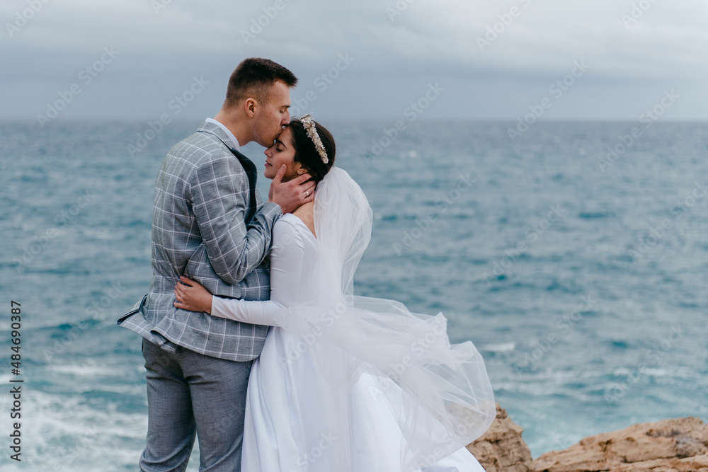 The newlyweds gently hug on the rocks by the sea and enjoy the nature of Cyprus