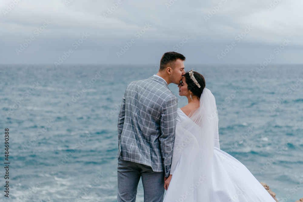 The newlyweds gently hug on the rocks by the sea and enjoy the nature of Cyprus