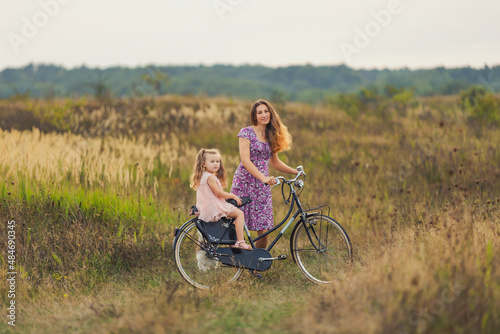 mother rides her daughter on a bicycle on a dirt road