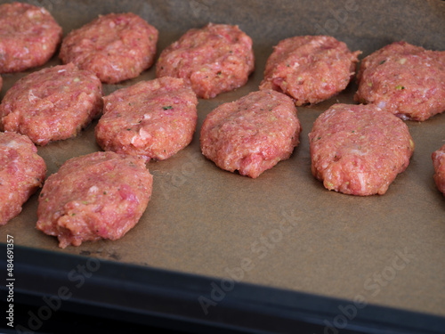 Raw meat cutlets on parchment paper in a baking sheet