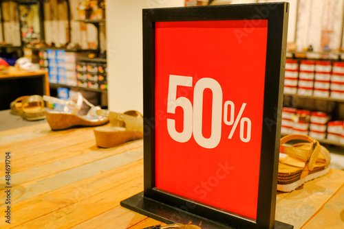 50 sales sign card in clothes store close-up across shelves with shoes and sneakers. Sales, discount, Black Friday, Cyber Monday, season sales concept. retail business
