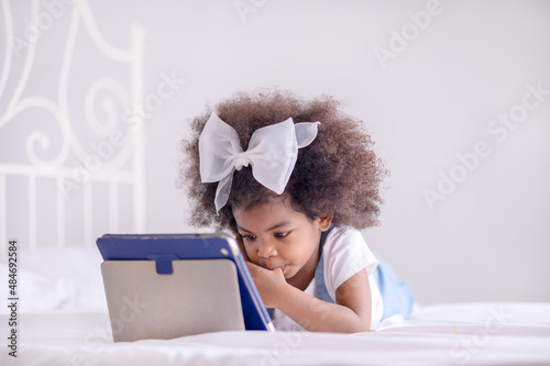 A half-African girl  lie in bed and watch online learning programs for kids on her mobile tablet