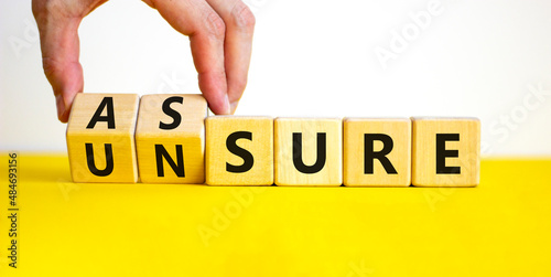 Assure or unsure symbol. Businessman turns wooden cubes and changes the concept word unsure to assure. Beautiful yellow table, white background, copy space. Business and assure or unsure concept. photo