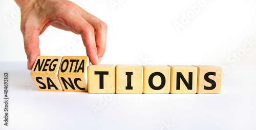 Sanctions or negotiations symbol. Businessman turns cubes, changes the word sanctions to negotiations. Beautiful white table, white background, copy space. Business, sanction or negotiation concept. photo