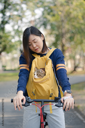 asian woman biking bicycle with her cat in backpack at park