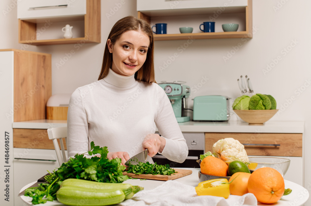 A young, beautiful vegetarian girl or blogger prepares breakfast of fruits, vegetables and greens at home in the kitchen. Blog about healthy eating