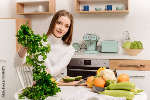 A young, beautiful vegetarian girl or blogger prepares breakfast of fruits, vegetables and greens at home in the kitchen. Blog about healthy eating