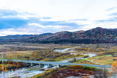 Railroad bridge crosses narrow river in highland in autumn