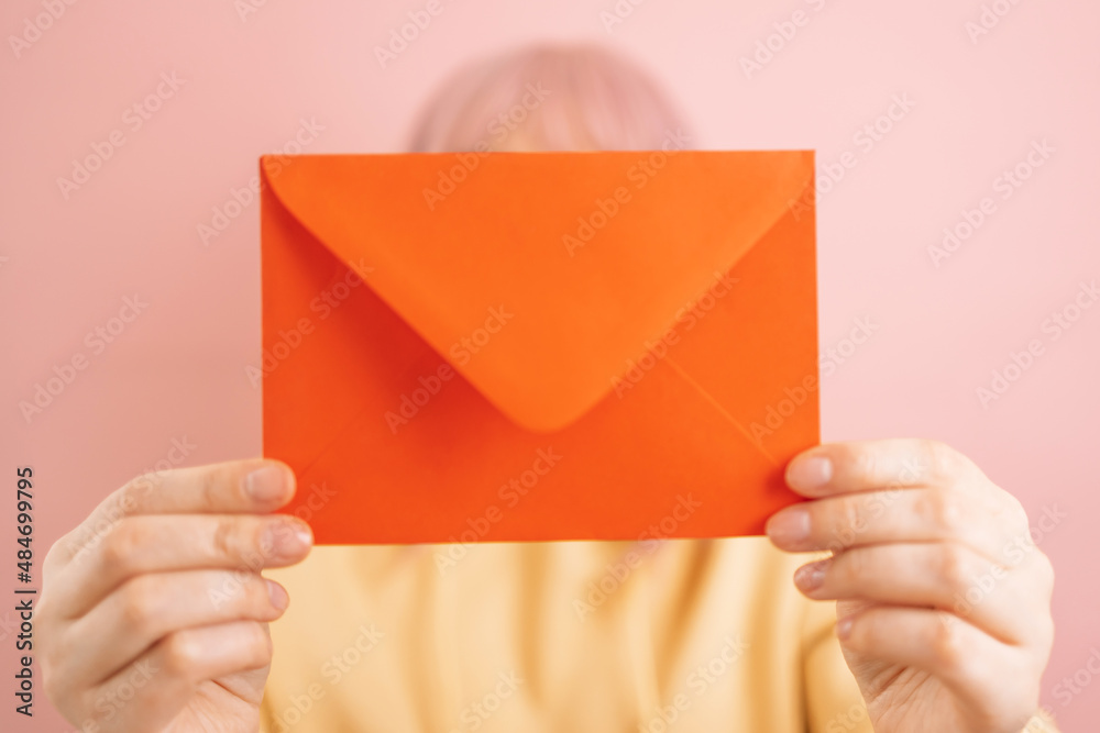 Woman hands holding red romantic envelope and looking at camera isolated on a pink background. Celebrating International Women Day, 8 march, mothers day, birthday.