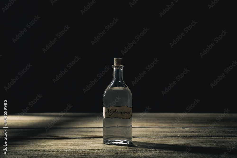 Magic potion on wooden table. Nightmares in the bottle. Corked bottle of mysterious liquid. Magic spells, potions and elixirs concept. Dark background... Magic potion on wooden table. Nightmares in the bottle. Corked bottle of mysterious liquid. Magic spells, potions and elixirs concept. Dark background...