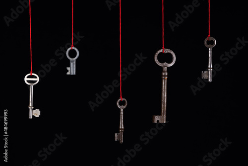 A lot of different old keys from different locks, hanging from the top on red strings. Finding the right key, encryption, concept. Retro vintage  keys on a dark background..