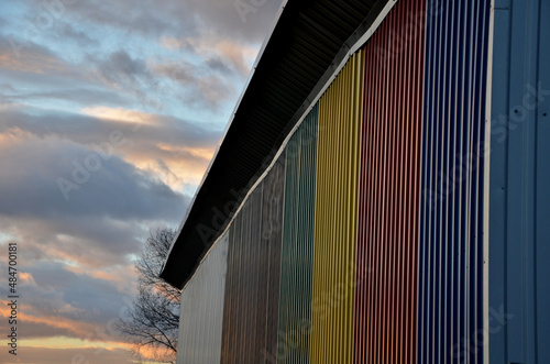 sheet metal wall of an industrial hall made of corrugated sheet metal in bright colors. Striped sheets complement the interestingly colored sky of the evening sky photo