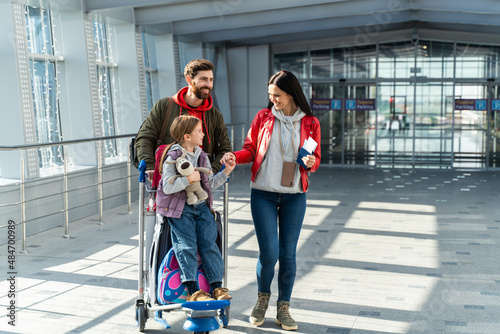 Father, mother and daughter getting ready for the flight while standing at departure lounge with suitcases and waiting for the aircraft arrival