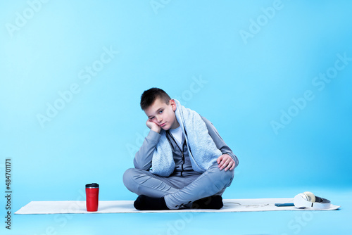 Exhausted teenage boy after a hard work-out, resting in his tracksuit on a yoga mat