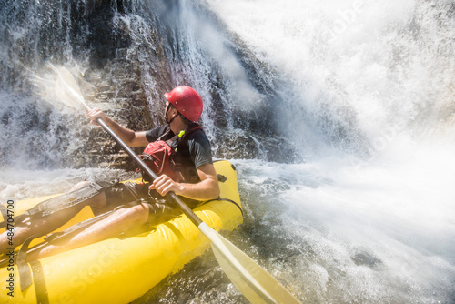 Paddler gets soaked while exploring river and waterfalls on raft. photo