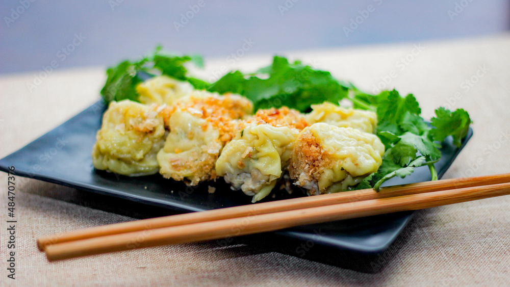 Chinese Steamed Dumpling served in a black plate on a wooden table. along with cilantro. Chinese Steamed Dumpling served in a black plate on a wooden table. along with cilantro.