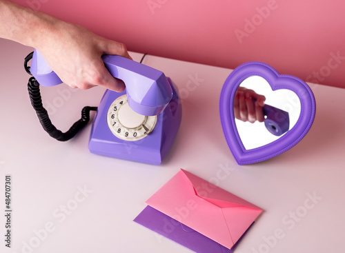 Woman hand holding retro phone handset. Vintage style telephone on table with heart-formed mirror and envelopes. Valentines day and love concept. High quality photo photo